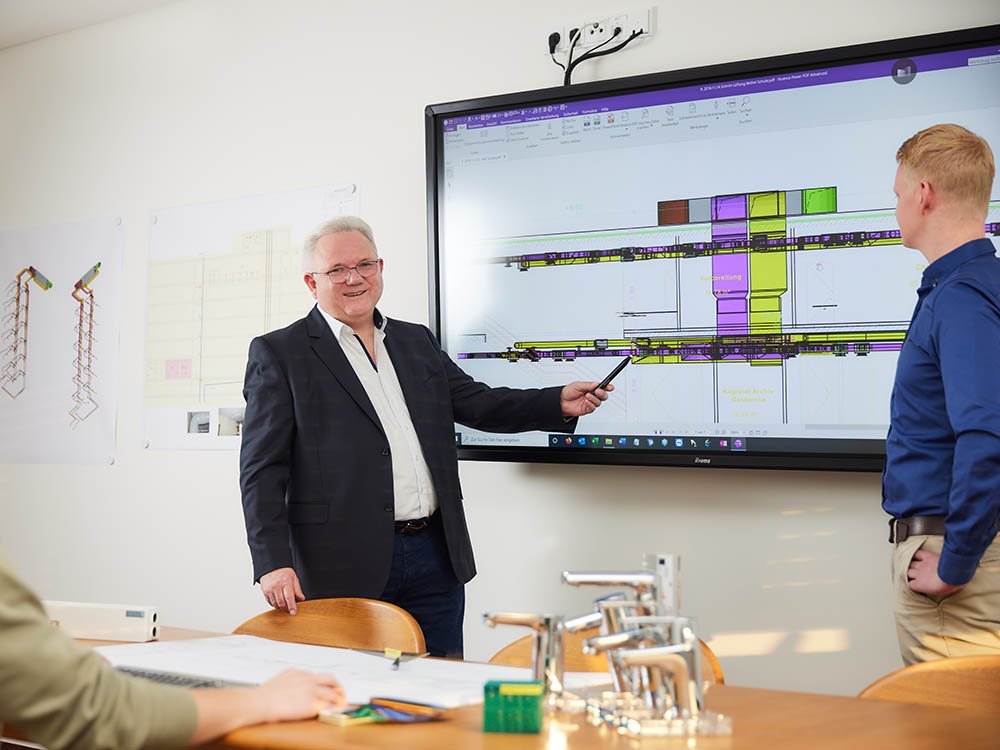 Teammeeting im Ingenieurbüro Klaus Reckmeyer mit Präsentation von TGA-Planung Besprechung technischer Gebäudeplanung mit digitalen CAD-Zeichnungen auf großem Bildschirm